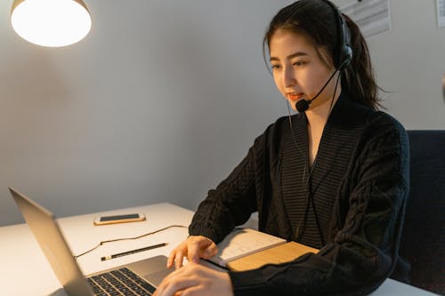 Free A Woman Wearing a Headset while Using Her Laptop Stock Photo