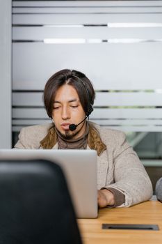 Focused young man in a headset working on a laptop in an office setting.