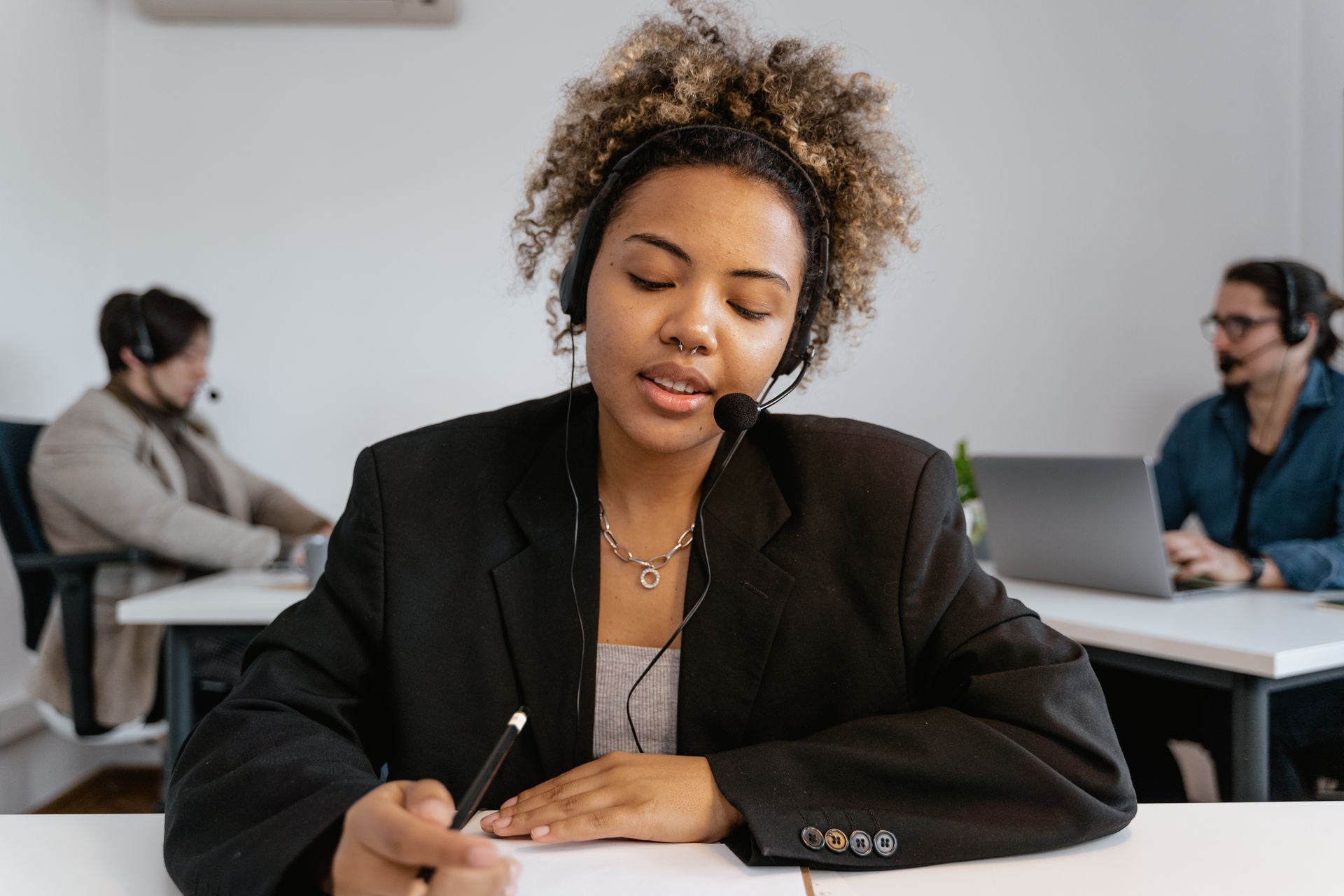 A Woman Wearing Black Blazer with Black Headset Holding a Pen