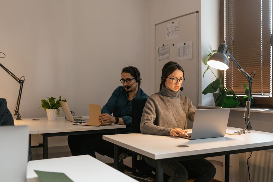 Two colleagues working in an office setting, focusing on laptops and customer support.