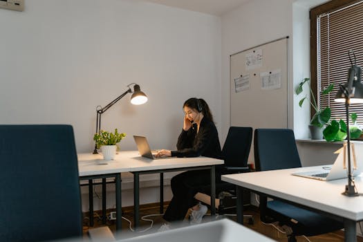 Professional woman with headset working in a bright office setting, focused on laptop.