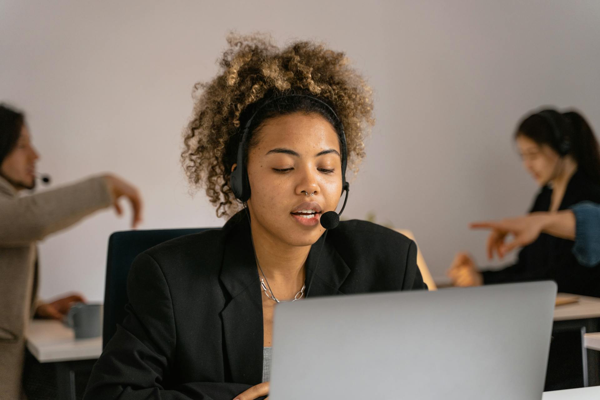 Customer support agent with headset working on laptop in office.