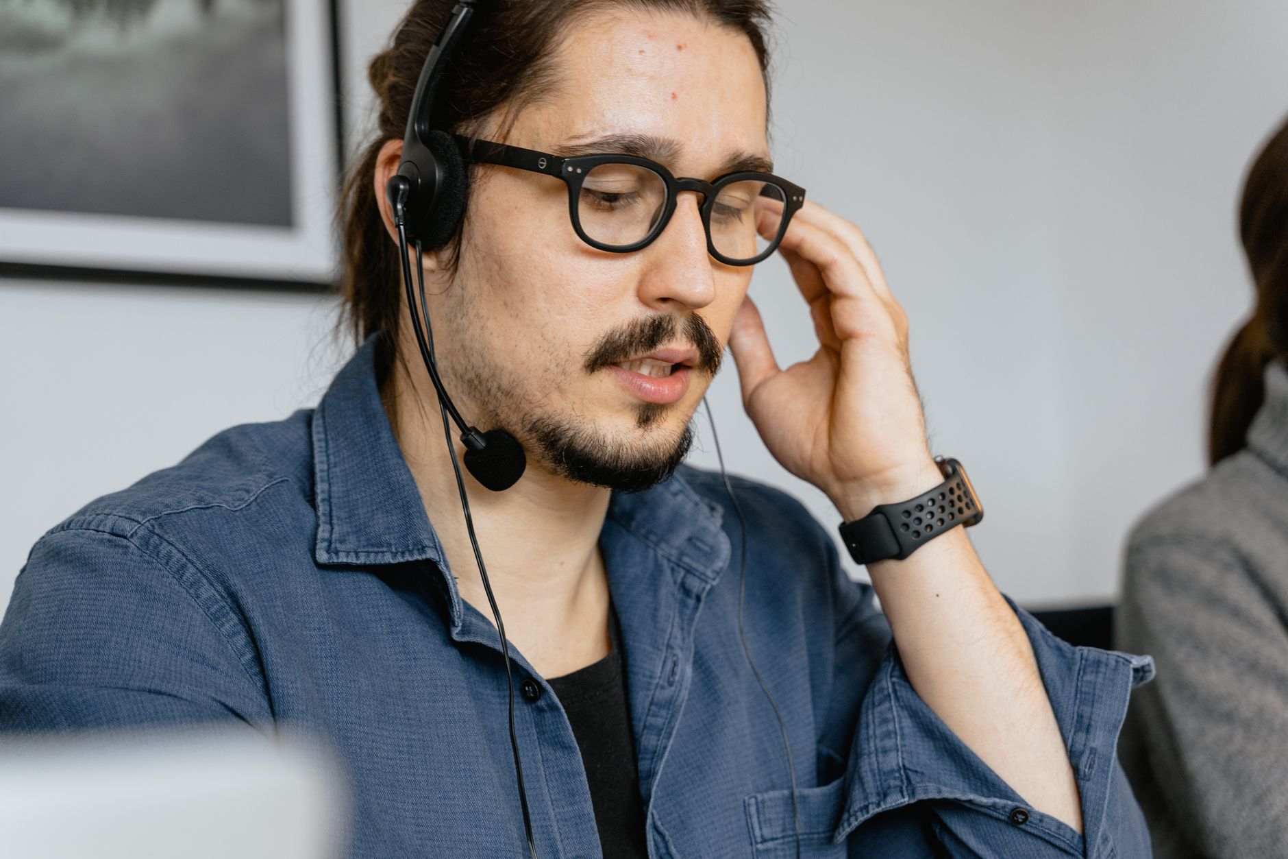 Un homme barbu avec des lunettes et des écouteurs travaillant dans un centre d'appels, fournissant un support client.