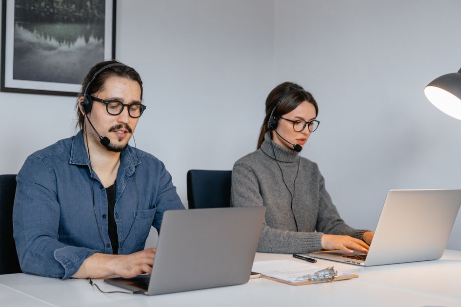 Deux personnes équipées de casques-micro répondent à des clients devant leurs ordinateurs portables dans un bureau.