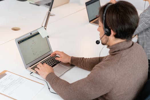 Call center agent wearing headphones working on a laptop in a modern office setting.