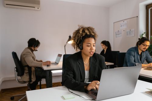 Free Professional team members with headsets working at laptops in a modern office setting. Stock Photo