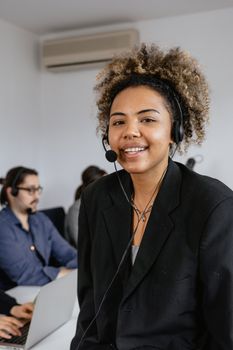Friendly call center agent with curly hair smiling, wearing a headset in an office