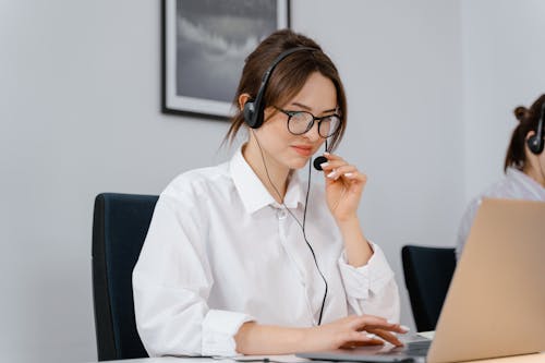 Photo of a Woman in a White Shirt Holding the Microphone on Her Headset