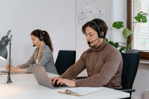 Free A Man in Brown Turtle Neck Shirt Using a Laptop and a Black Headset Stock Photo