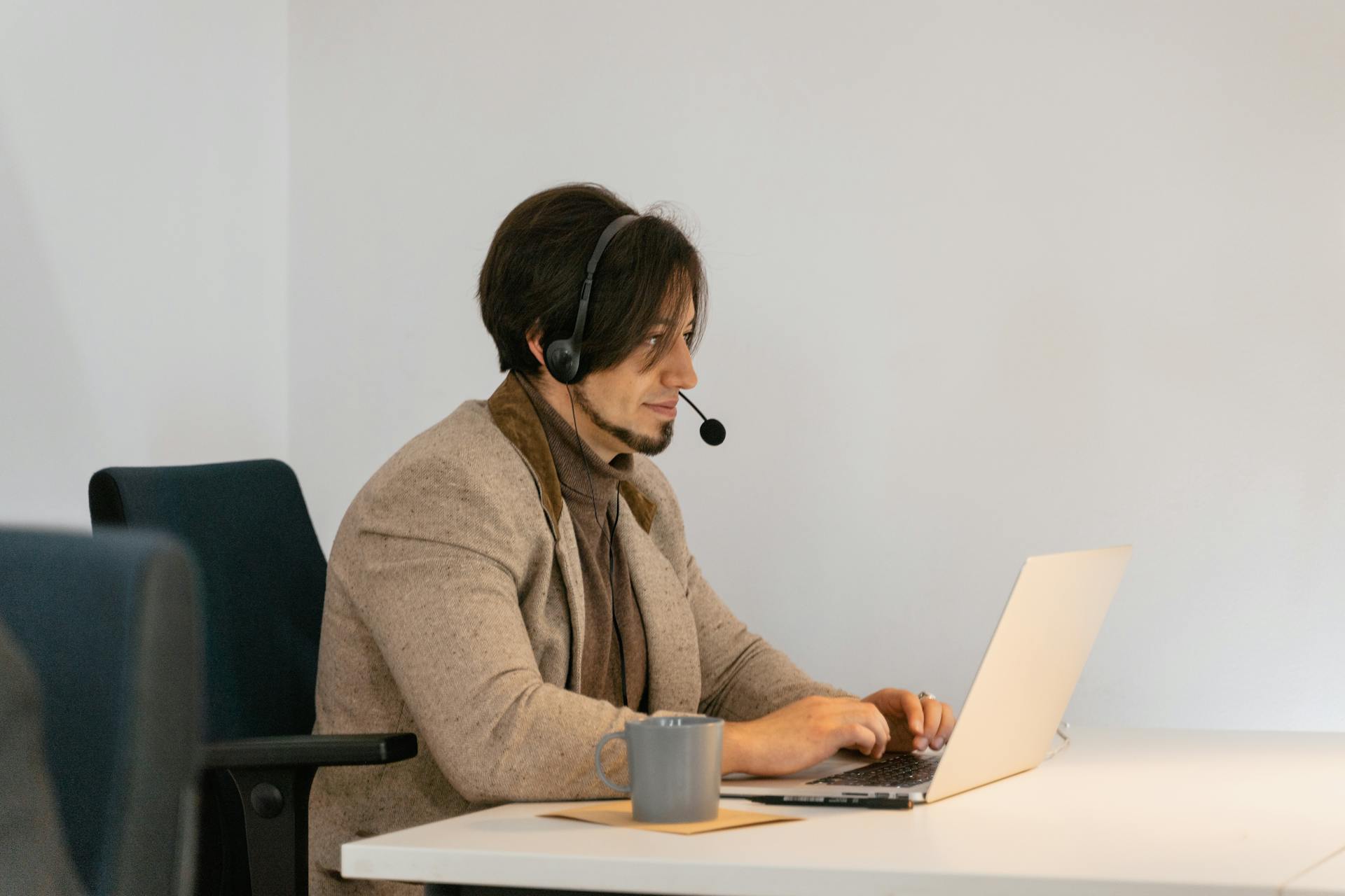 Man with headset typing on laptop in a modern office setting, providing customer support.