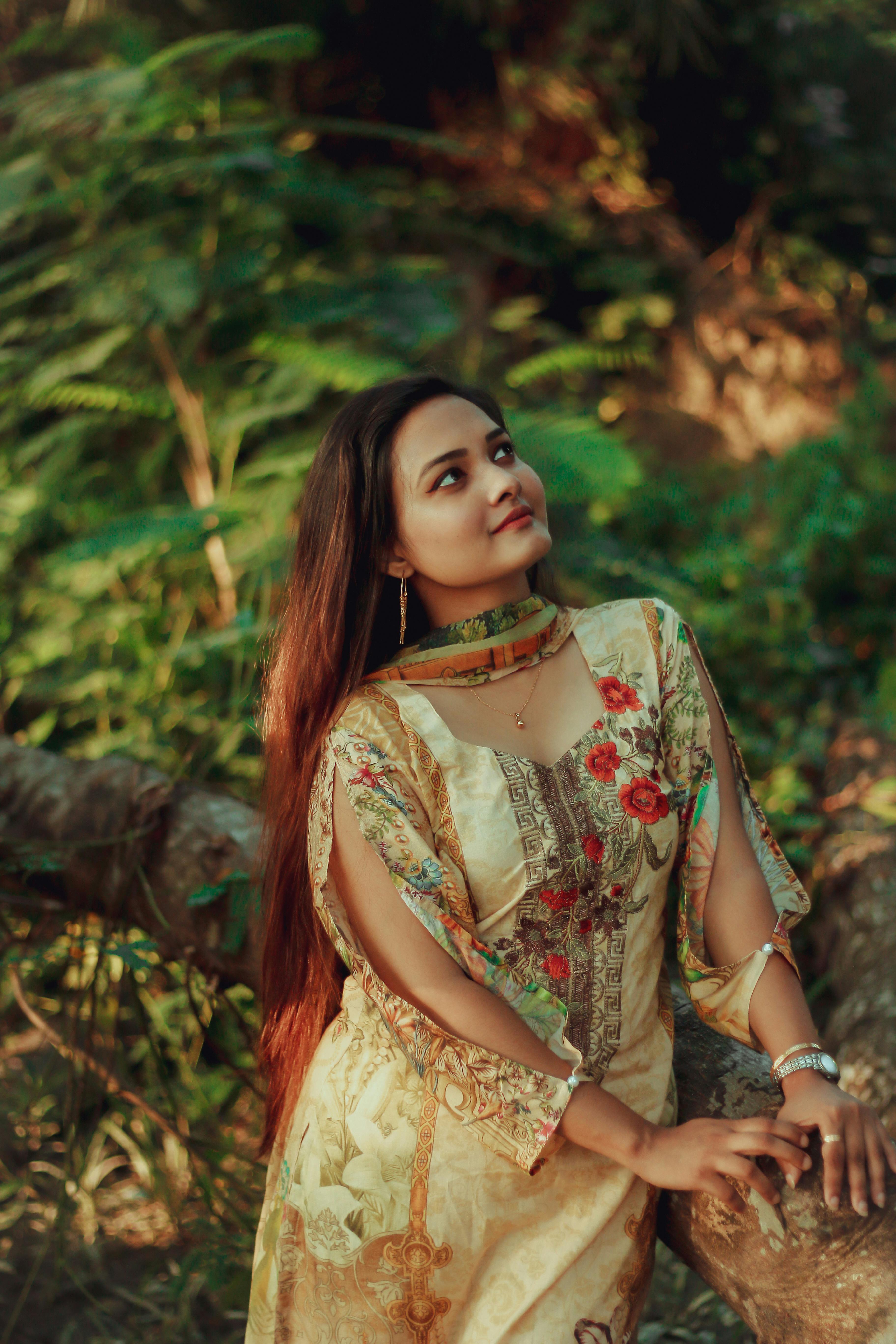 Asian woman in a floral dress looking serene in a lush outdoor setting.