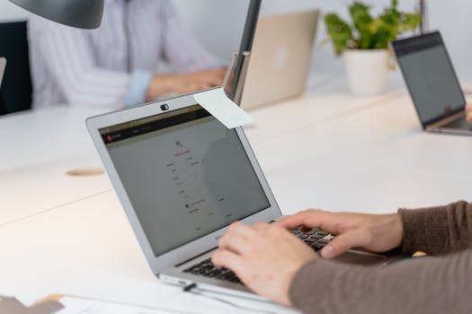 Close-up of a professional working on a laptop with a sticky note in a modern office setting.