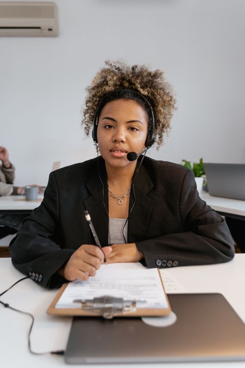 Free Woman in professional office setting using a headset and clipboard, focused on customer service. Stock Photo