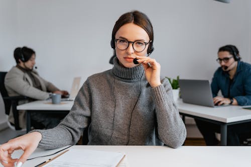 Woman in a Gray Sweater Holding the Microphone of Her Headset