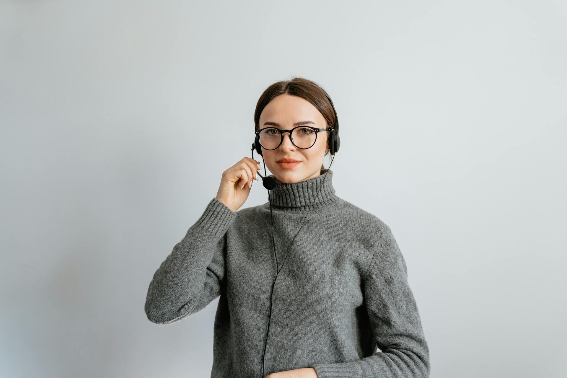 Caucasian woman in gray sweater and glasses providing customer support using a headset in an office.