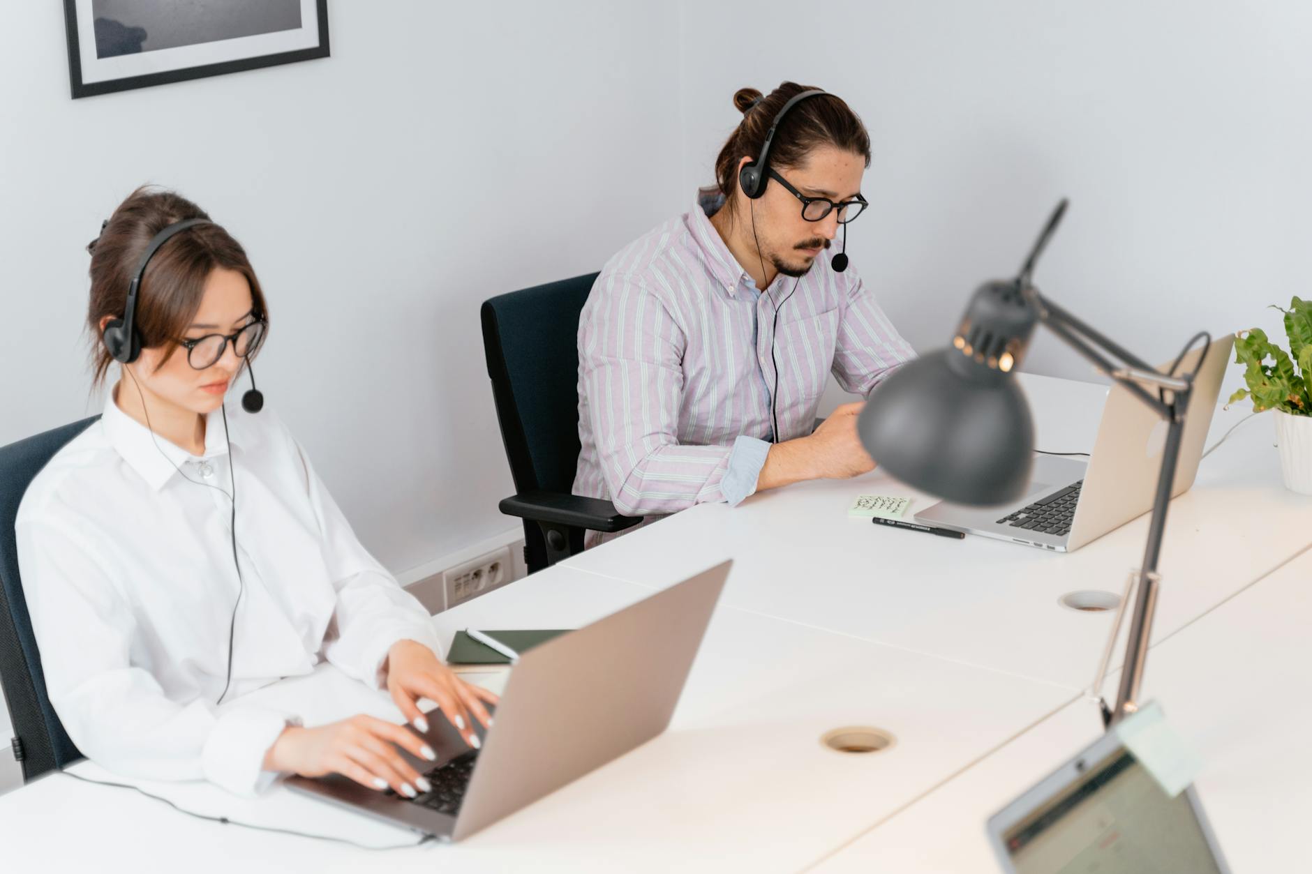 Two office workers focusing on tasks at a call center, using laptops and headsets.
