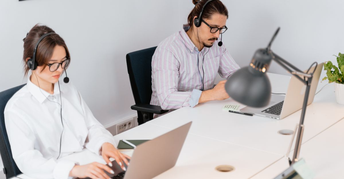 Two office workers focusing on tasks at a call center, using laptops and headsets.