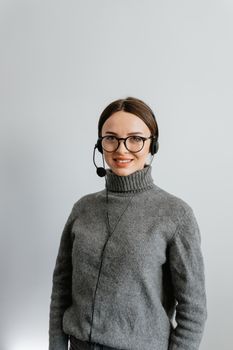 Portrait of a smiling woman with eyeglasses and a headset in a gray turtleneck, perfect for customer support themes.