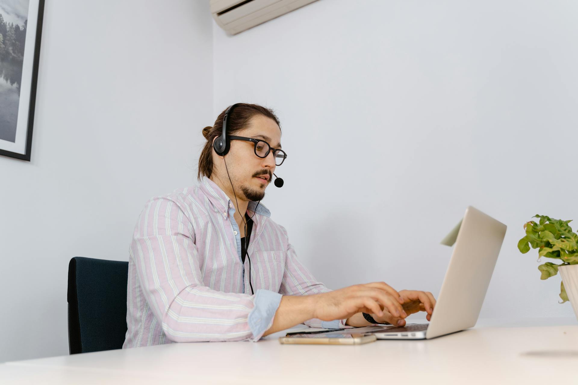 Man working in office with laptop, wearing a headset for customer support.