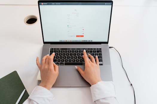 Close-up of hands typing on a laptop in a modern office environment.