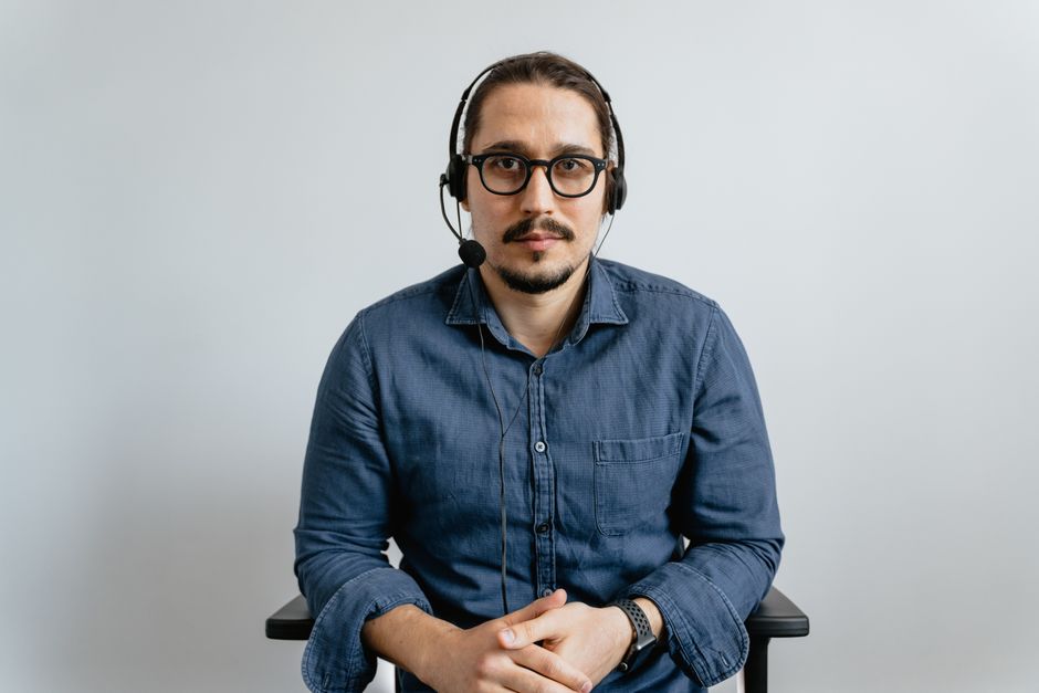 Support agent wearing headset and glasses in office setting, providing customer service. Support agent wearing headset and glasses in office setting, providing customer service.