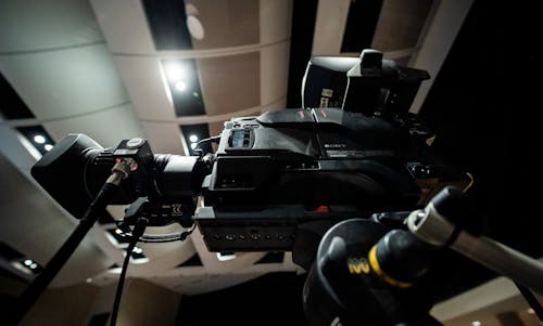 Contemporary professional video camera with lens placed on tripod under ceiling with lights in modern studio