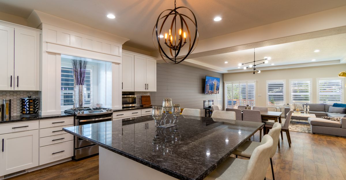 Open-concept kitchen featuring white cabinets, a dark granite island, and an orb chandelier.