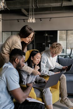 Diverse group of young professionals collaborating on laptops in a modern office setting.