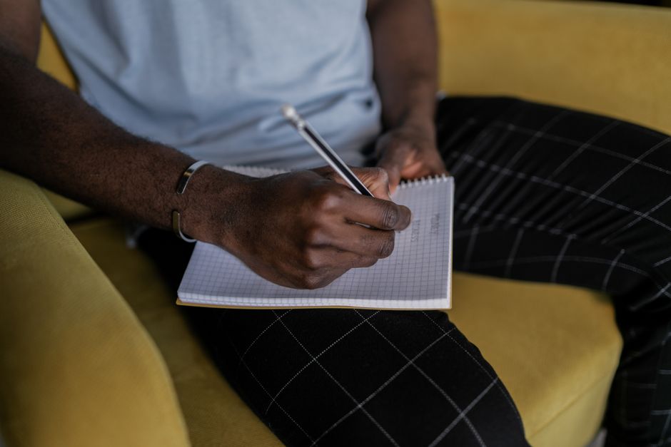 Close-up of a man writing in a notebook with a pencil while sitting on a yellow armchair. Close-up of a man writing in a notebook with a pencil while sitting on a yellow armchair.