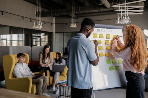 Free Team collaborating in a modern office, planning strategy on a whiteboard, young adults working together. Stock Photo