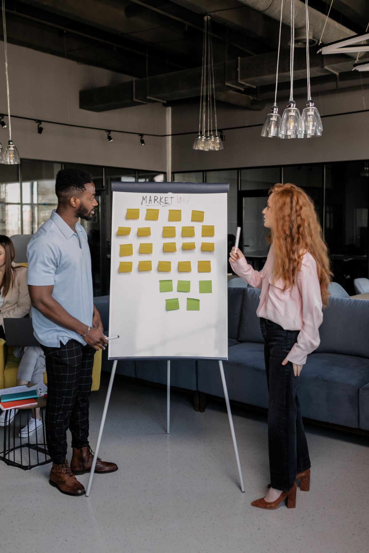 Two colleagues planning a marketing strategy with sticky notes on a whiteboard