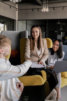 Three young professionals collaborate in a modern office setting with laptops.