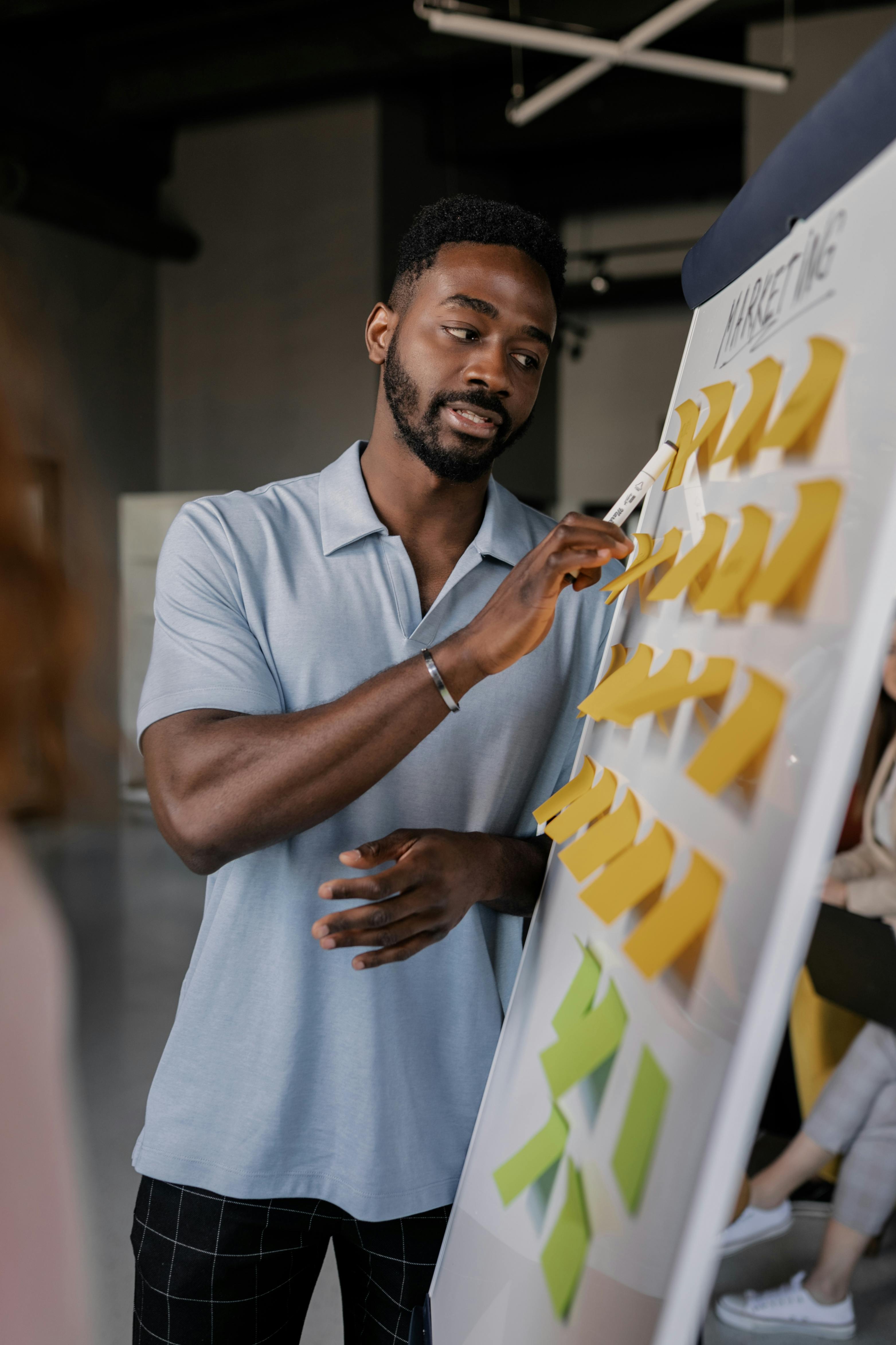 man in a blue shirt pointing to a whiteboard with sticky notes