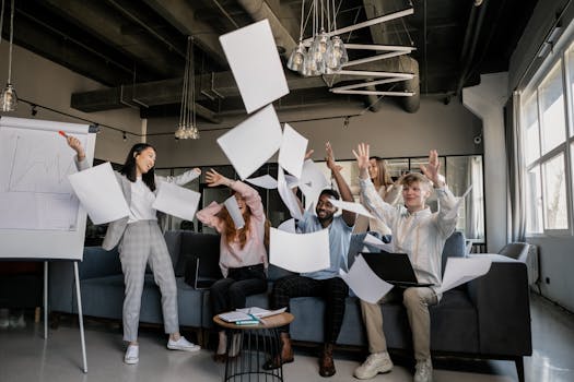 A diverse team of adults celebrates success with papers flying in an office setting.