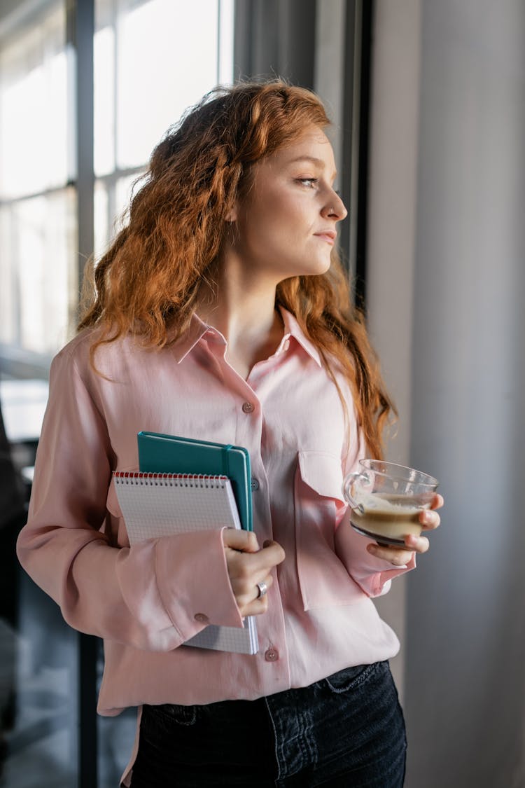 A Woman With Red Hair Looking Away While Holding A Cup Of Coffee