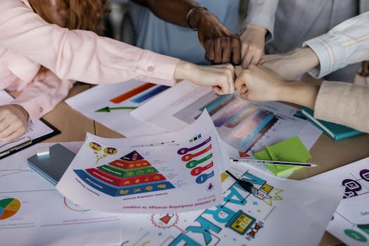 A diverse team unites hands over business reports and marketing strategies, symbolizing teamwork.