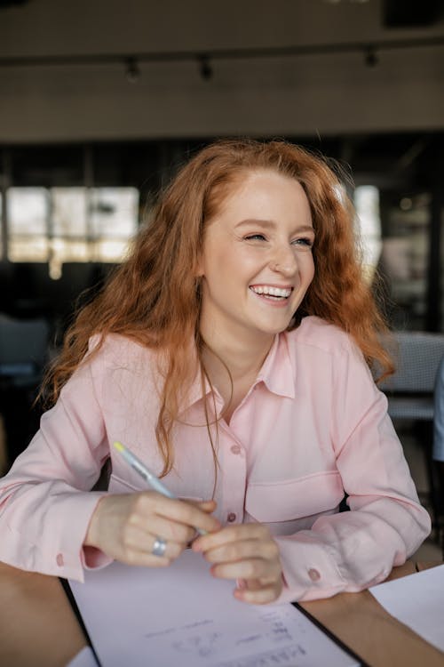 Free Close-Up Photo of a Woman with Red Hair Laughing while Holding a Pen Stock Photo