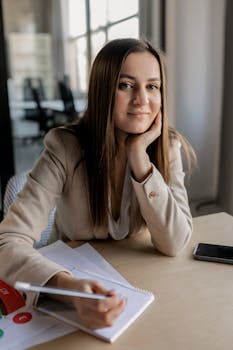 Businesswoman sitting at desk in modern office, holding pen, with files and smartphone.