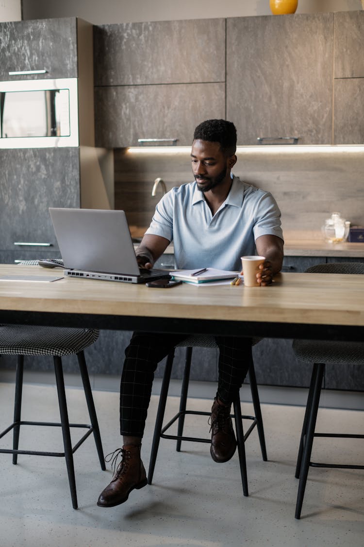 Man In Blue Polo Shirt Working At A Laptop In A Kitchen