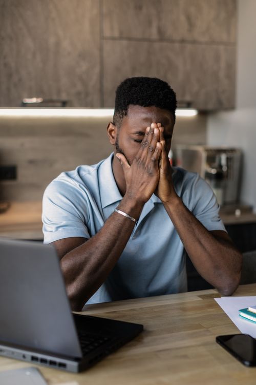 Free Man sitting at desk with laptop, showing frustration during work in modern office setting. Stock Photo