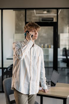 Caucasian man talking on smartphone at office desk, modern workspace.