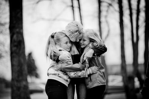 Grayscale Photo of a Mother Hugging Her Daughters