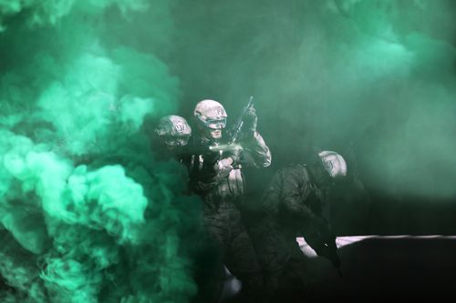 Free Three soldiers emerge from green smoke in a tactical military operation. Stock Photo