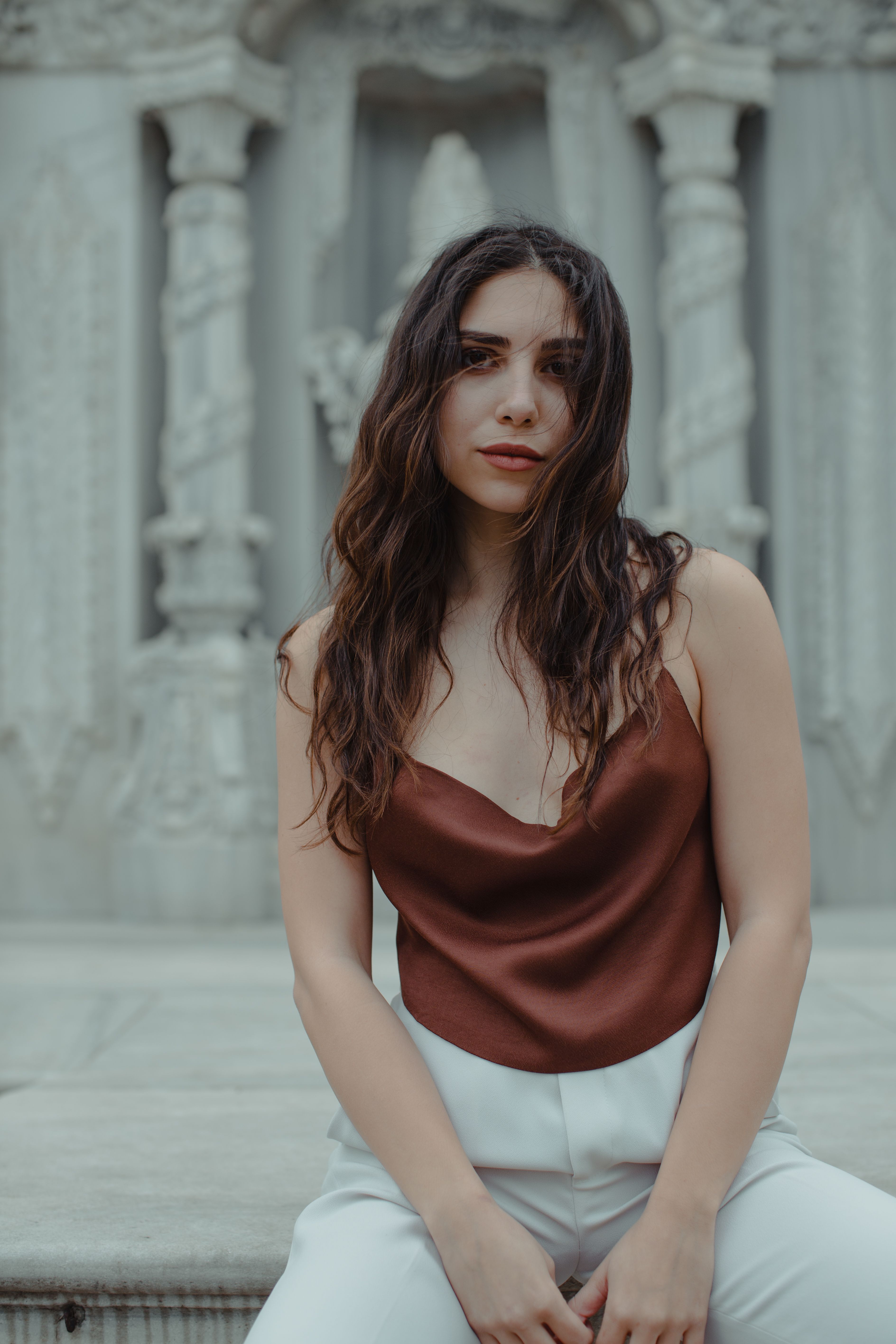 Long haired female looking at camera while sitting on terrace in front of marble bas relief