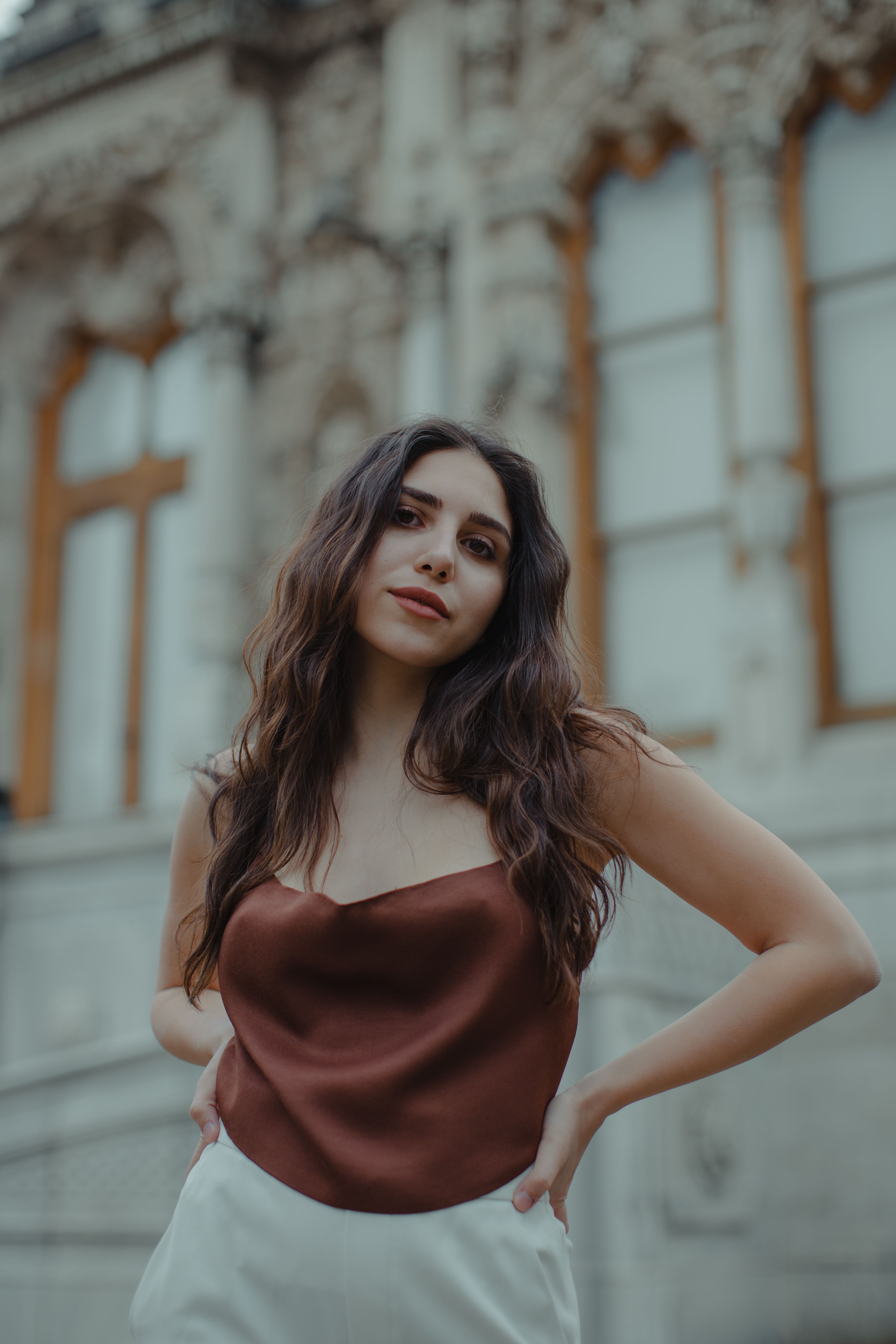 Portrait of a stylish woman with long hair posing outdoors against decorative building facade.