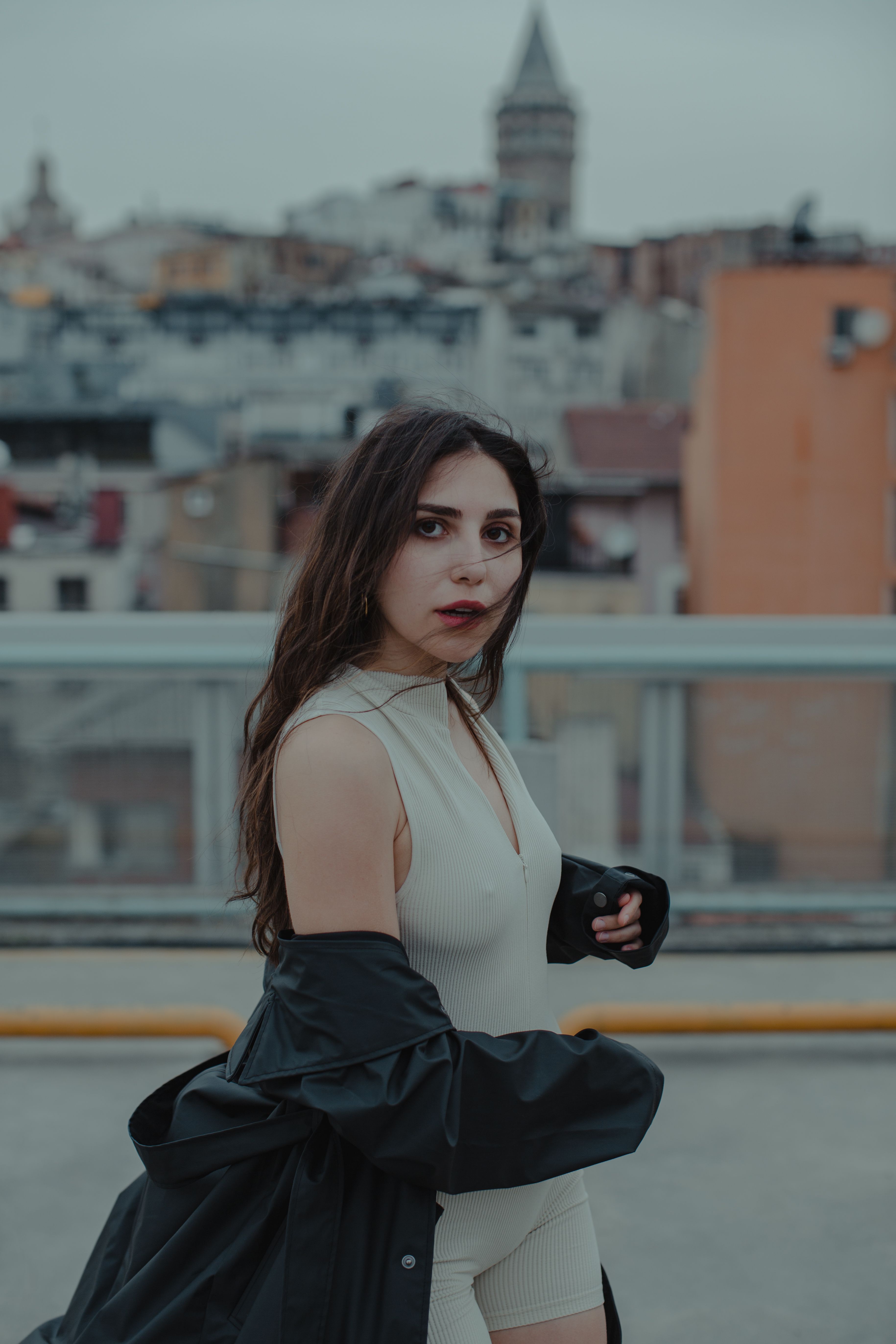 Fashionable woman standing in front of Galata Tower, Istanbul with a modern cityscape backdrop.
