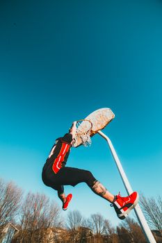 Full body side view of anonymous sportive male in activewear hanging on basketball hoop while playing on sports ground against blue sky on sunny street