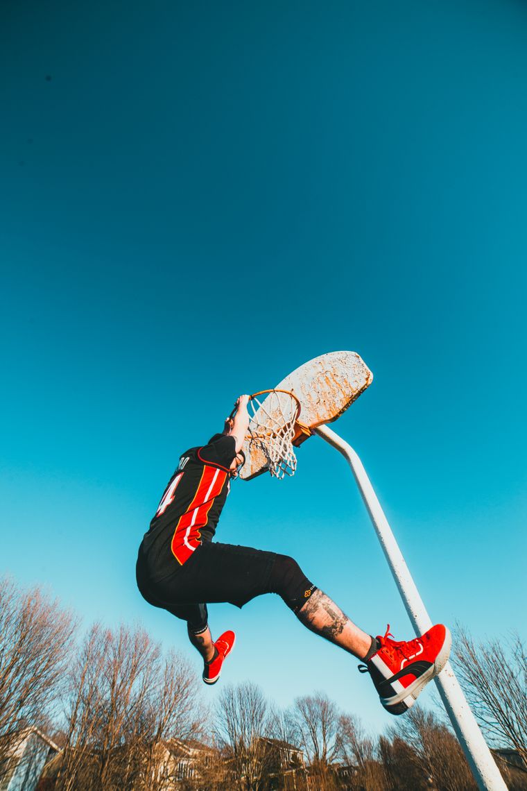 Player in activewear hanging from a basketball hoop — photo by Erik Mclean on Pexels