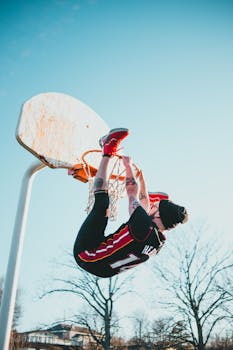 Man in activewear hangs from a basketball hoop in an outdoor court, showcasing a dynamic sports pose.