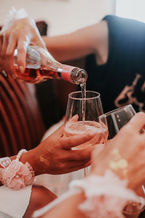 Free Crop anonymous woman pouring sparkling wine from bottle into glass of female friend during bridal shower party Stock Photo